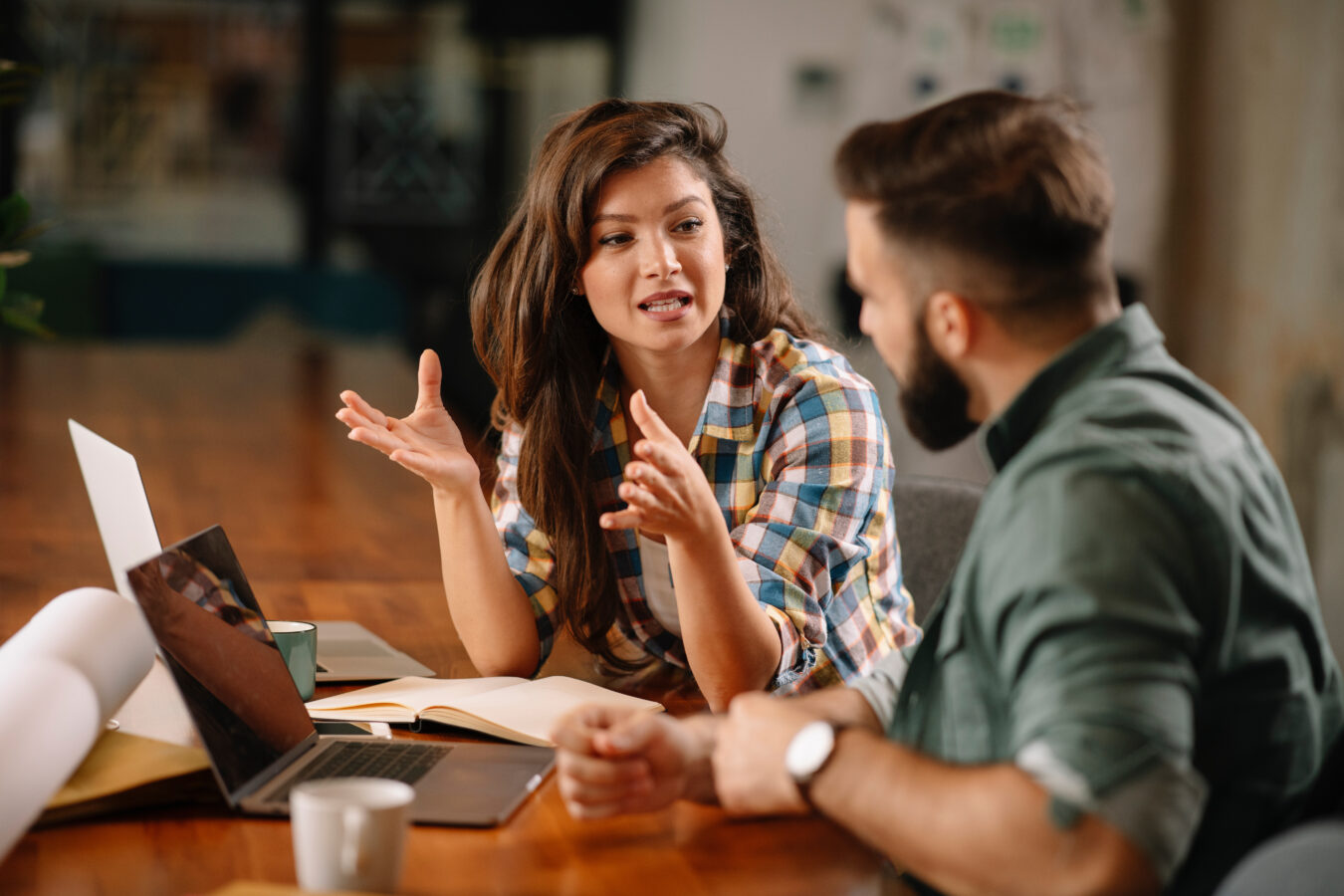 A woman and a man talk at a table with computers