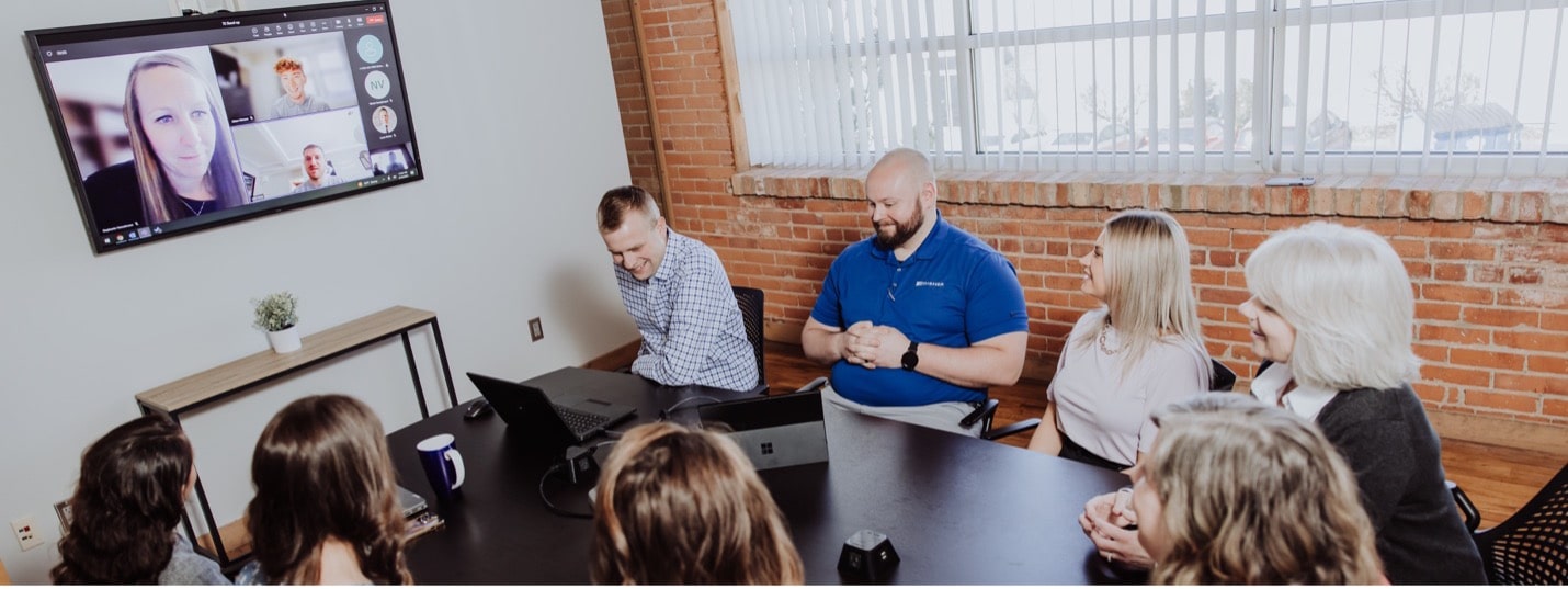 A team of sits around a conference table while talking to other team members working remotely.